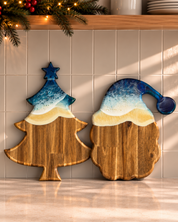 Two wooden holiday serving boards with a blue and white frosted top design, one shaped like a Christmas tree and the other like a Santa hat, displayed on a kitchen counter.