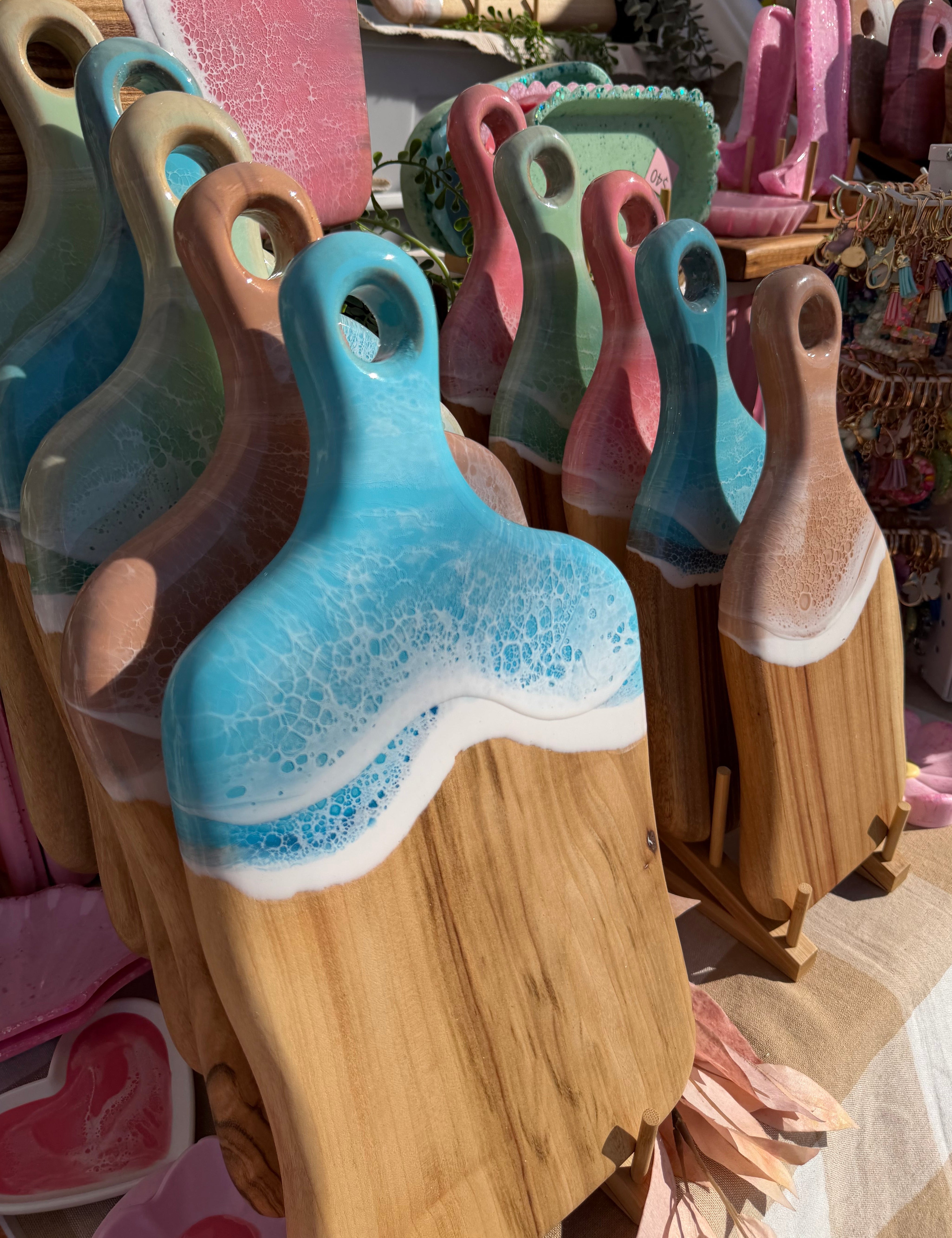 Close-up of the pastel ocean waves resin detail on medium paddle cheeseboards at a market, camphor laurel timber