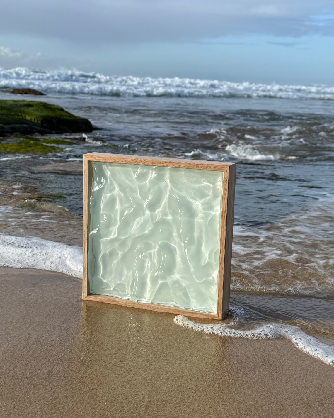 Art of Elements Salt Air Bahamas 3D sculptured resin art piece the looks like frozen water, in a wooden frame standing on a sandy beach by the ocean