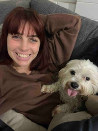 Woman with auburn hair smiling next to a small white dog on a sofa