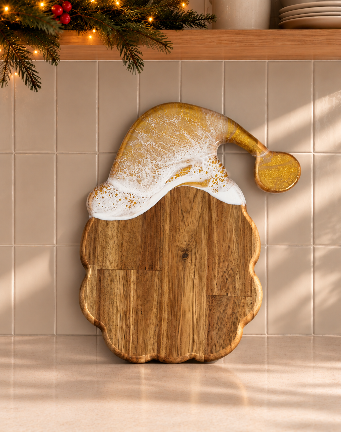 A wooden Santa hat shaped serving board with a gold glittery hat and white faux foam trim, displayed against a beige tiled wall with holiday greenery and string lights above.