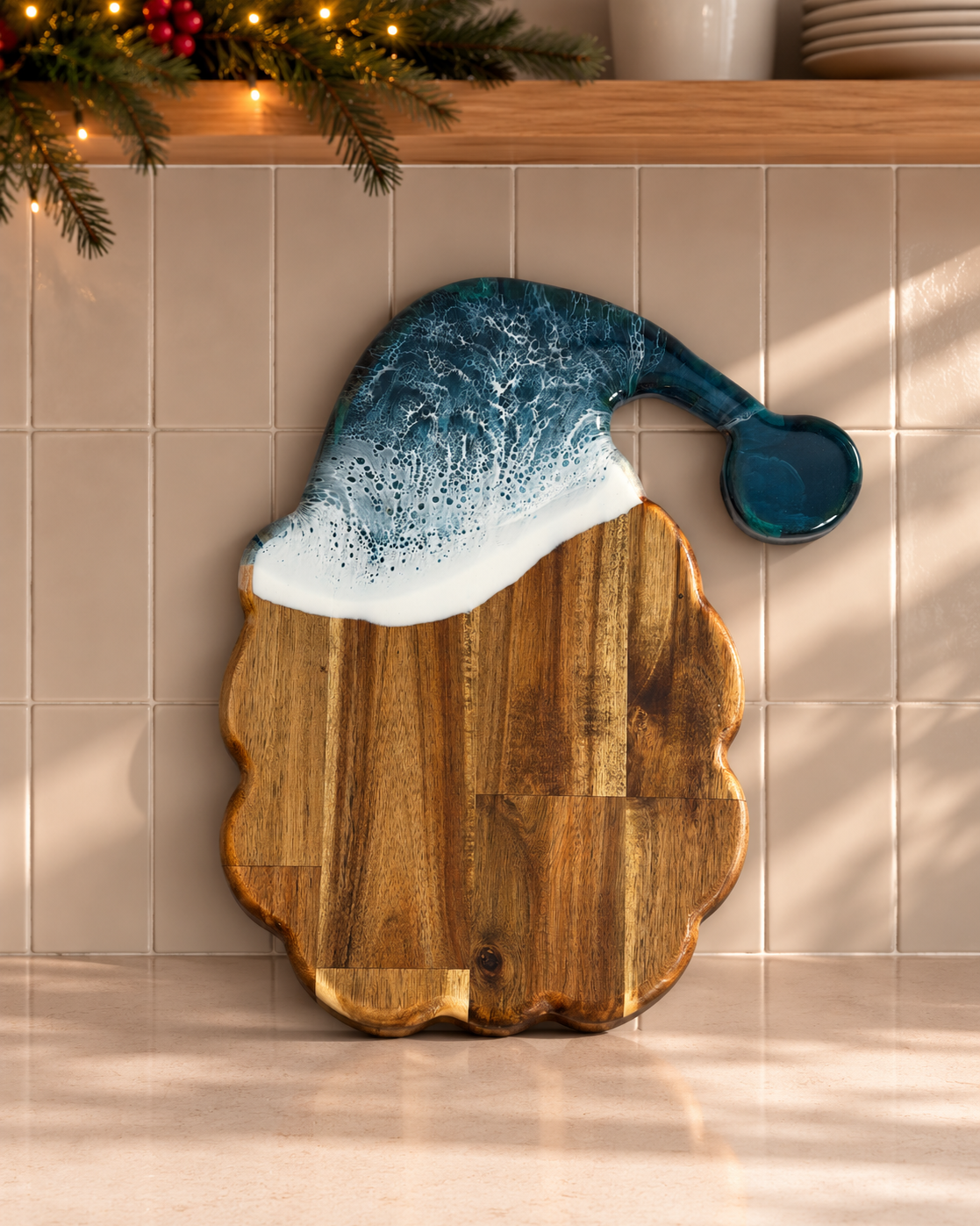 A wooden Santa hat shaped serving board with a scalloped edge, featuring a dark blue glazed hat topper with white faux snow and a small matching blue spoon in a holiday kitchen setting.