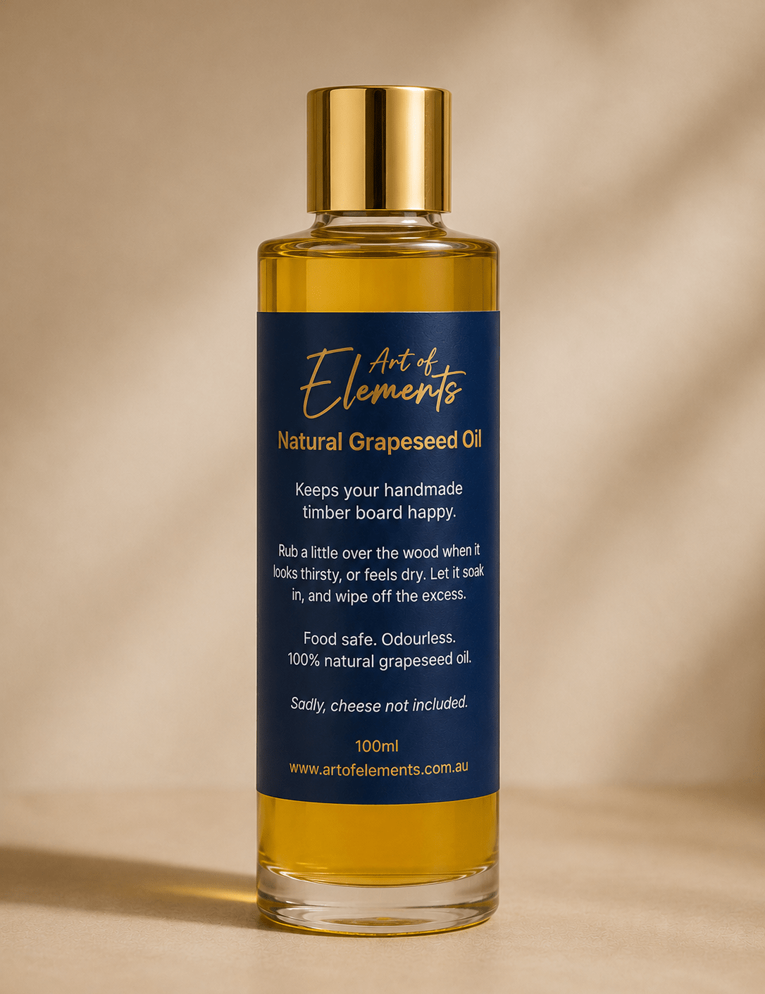 A 100ml bottle of Art of Elements Natural Grapeseed Oil with a gold cap and a navy blue label, set against a warm beige background with soft shadows.