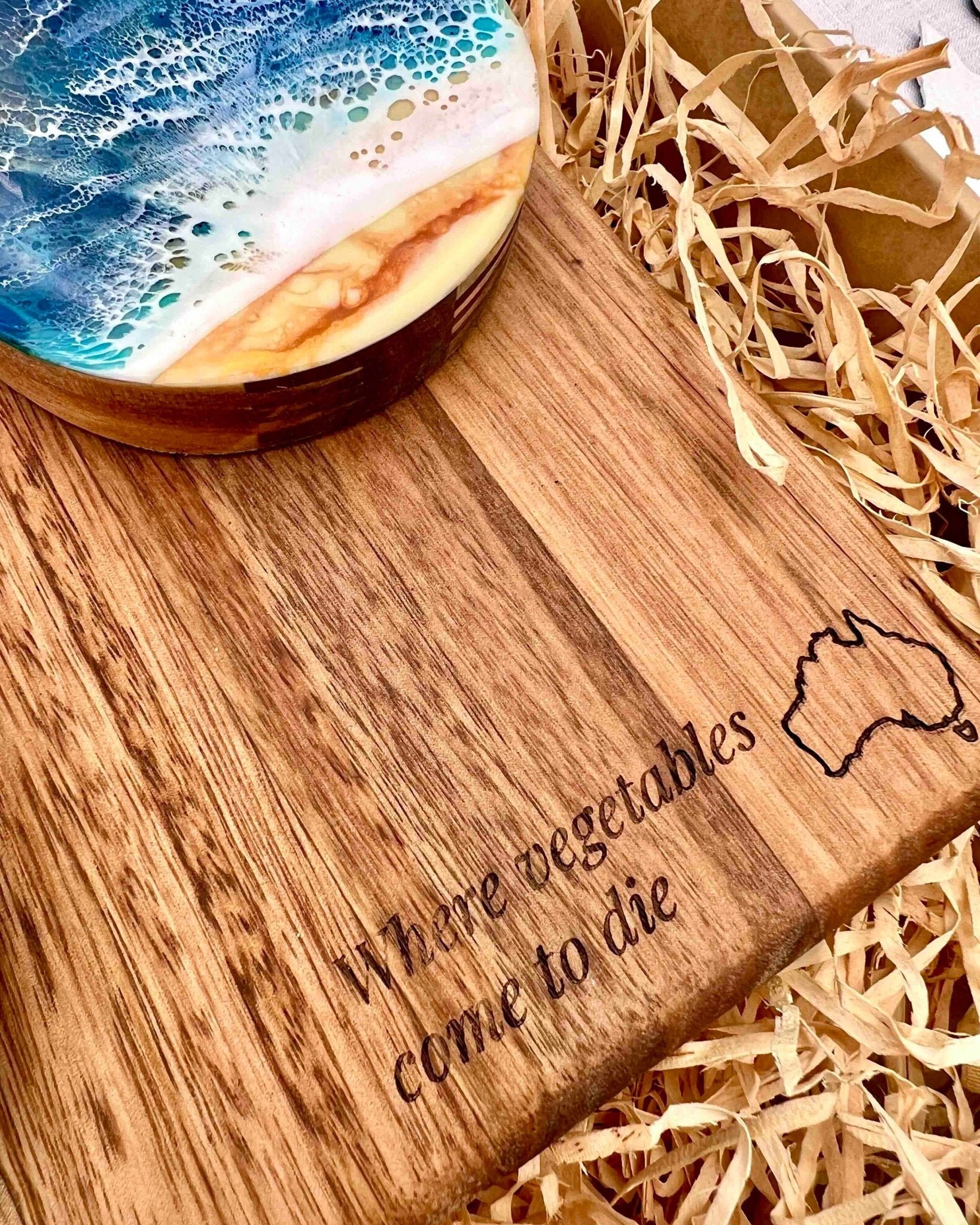 A close-up of a wooden cutting board engraved with the phrase 'Where vegetables come to die' and a simple outline of Australia