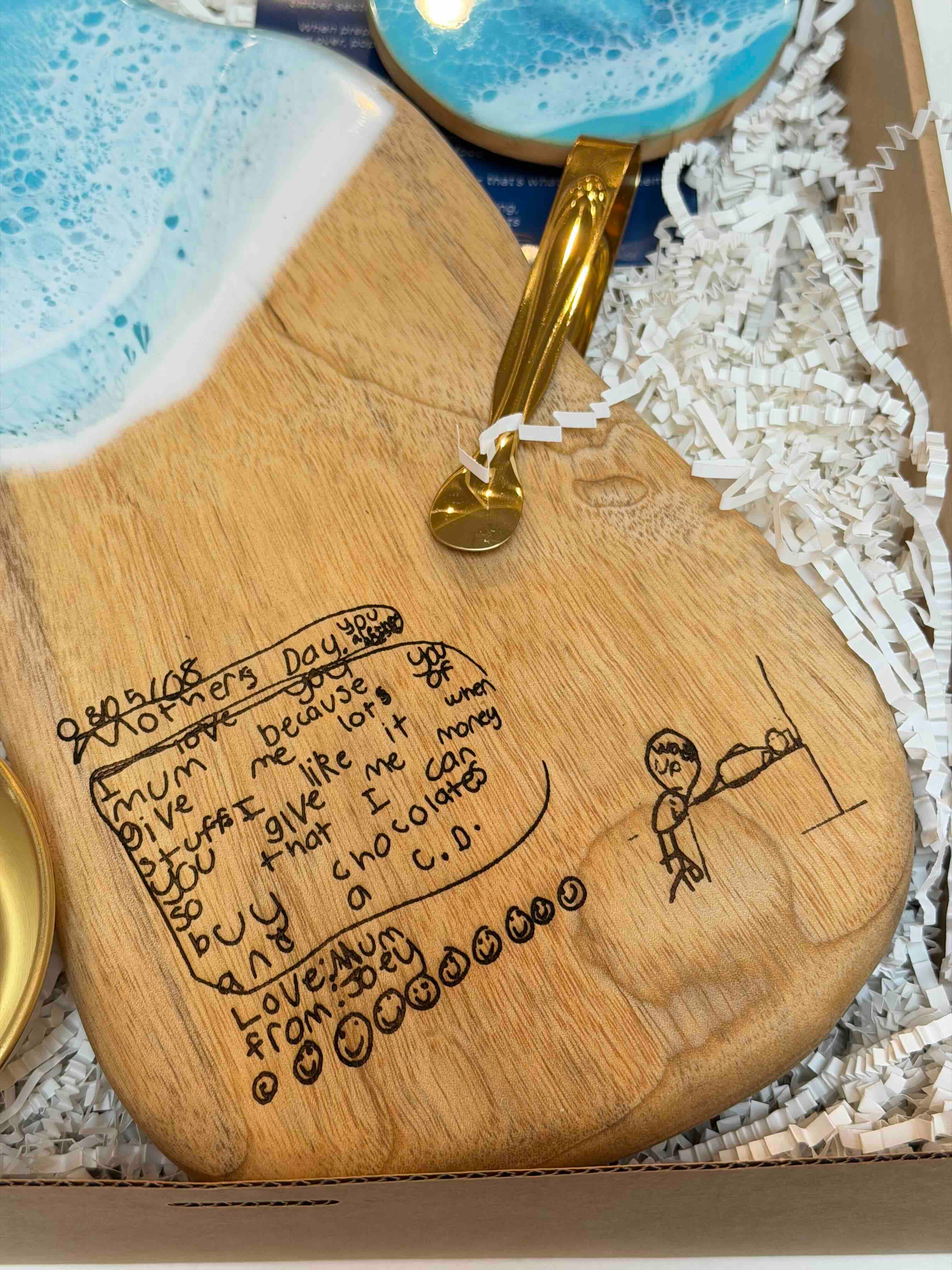 Wooden serving board with engraved child handwriting and gold serving tongs in gift box