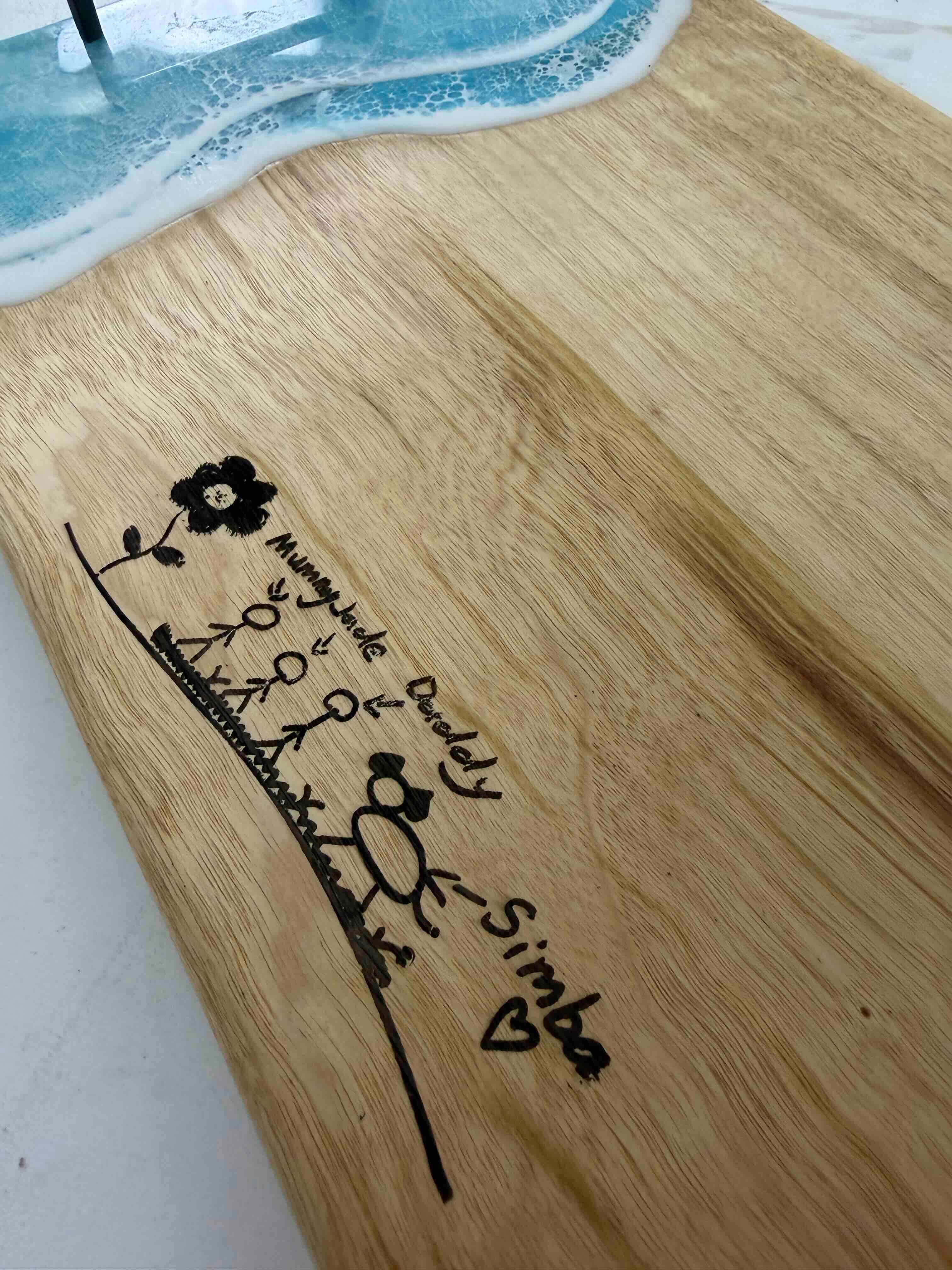 Wooden serving board with blue resin ocean wave detail and custom laser engraved family stick figure drawing
