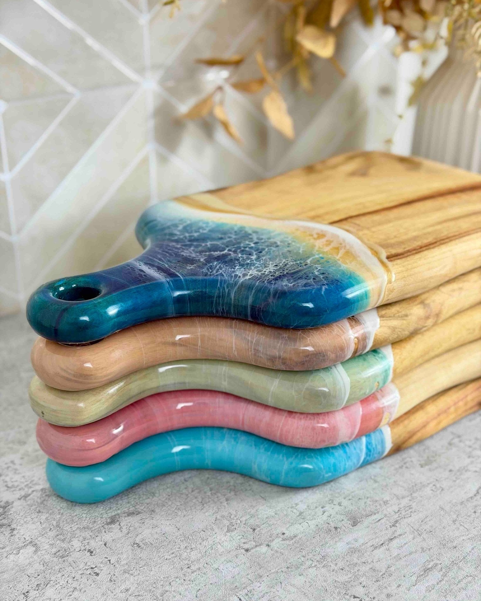 Stack of colourful epoxy resin chopping boards. The resin rolls over the edge of each board perfectly covering the camphor laurel timber edge 
