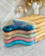 Stack of colourful epoxy resin chopping boards. The resin rolls over the edge of each board perfectly covering the camphor laurel timber edge 
