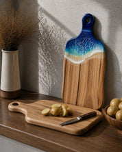 The back of the cutting board with a knife and potatoes on a camphor laurel surface, with the same board with the resin facing the front, leaning against the kitchen wall. Designed for function and style.