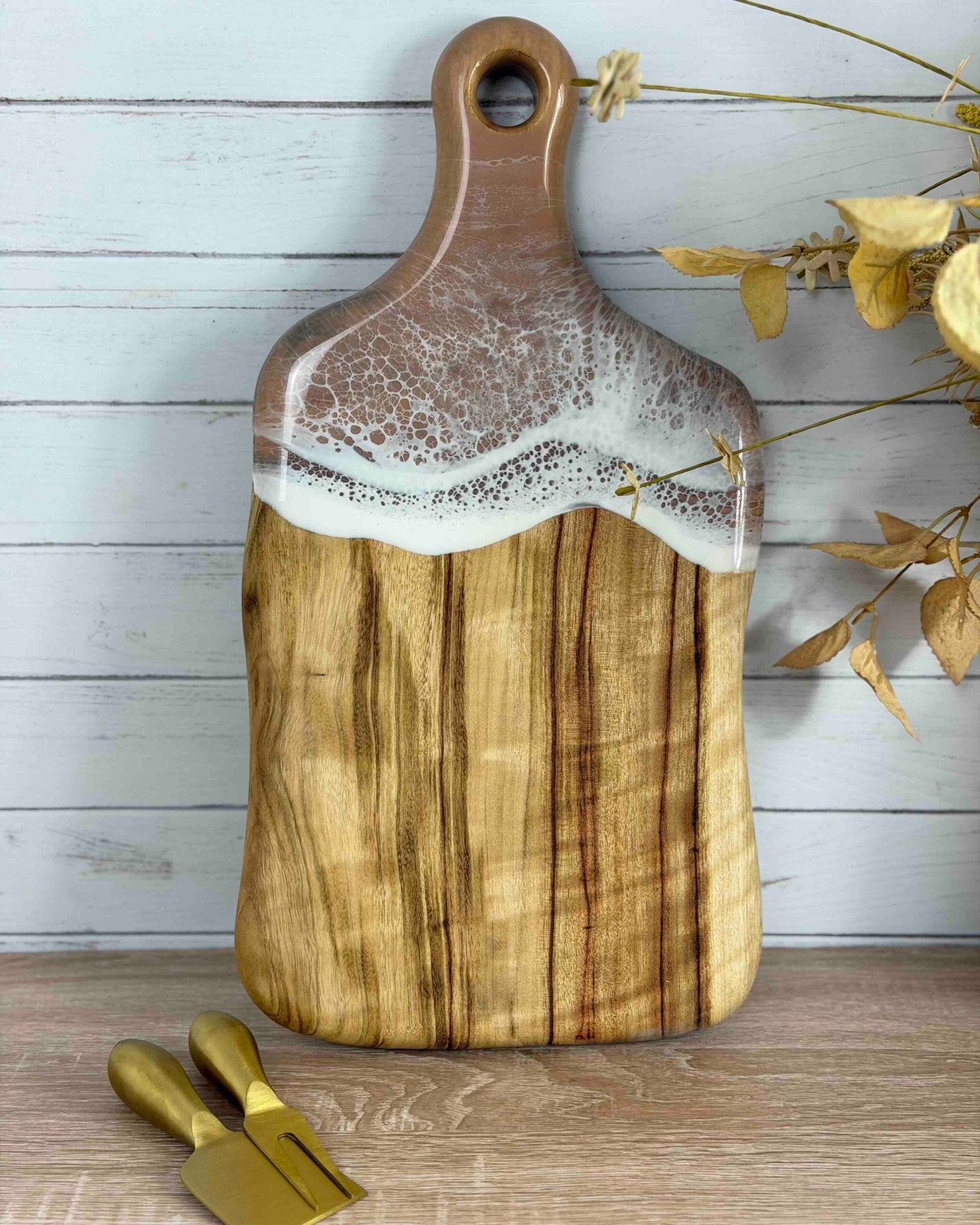 Timber cutting board with a a subtle resin beige waves and gold tools on a wooden surface.