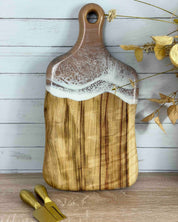Timber cutting board with a a subtle resin beige waves and gold tools on a wooden surface.