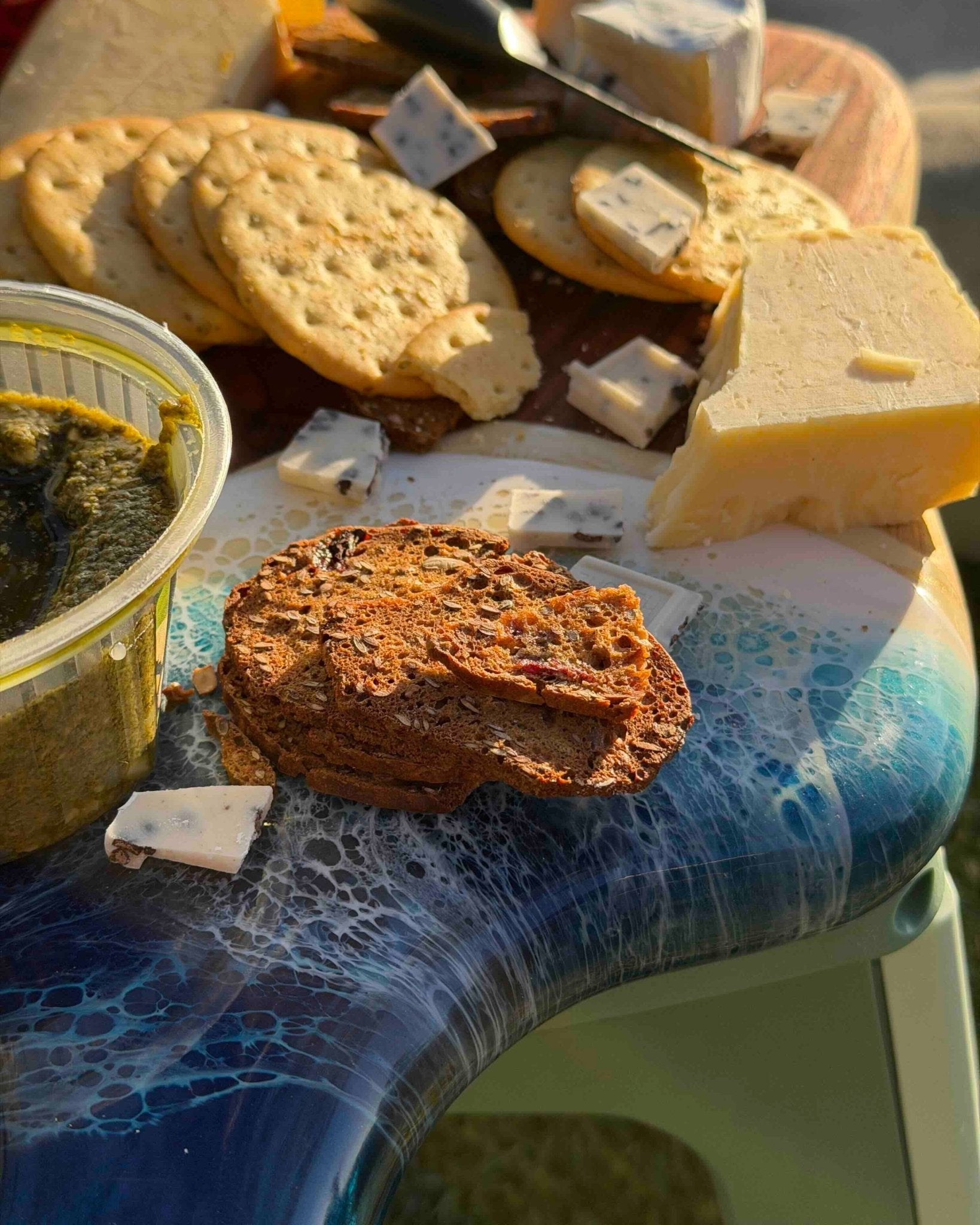 Assorted cheese and crackers on a close up shot of the resin waves on the handle of the handmade cheeseboard