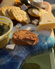 Assorted cheese and crackers on a close up shot of the resin waves on the handle of the handmade cheeseboard