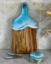 Camphor laurel naturally antibacterial cutting board with a light blue wave design on a tiled wall background, matching coasters sitting in front of the board 