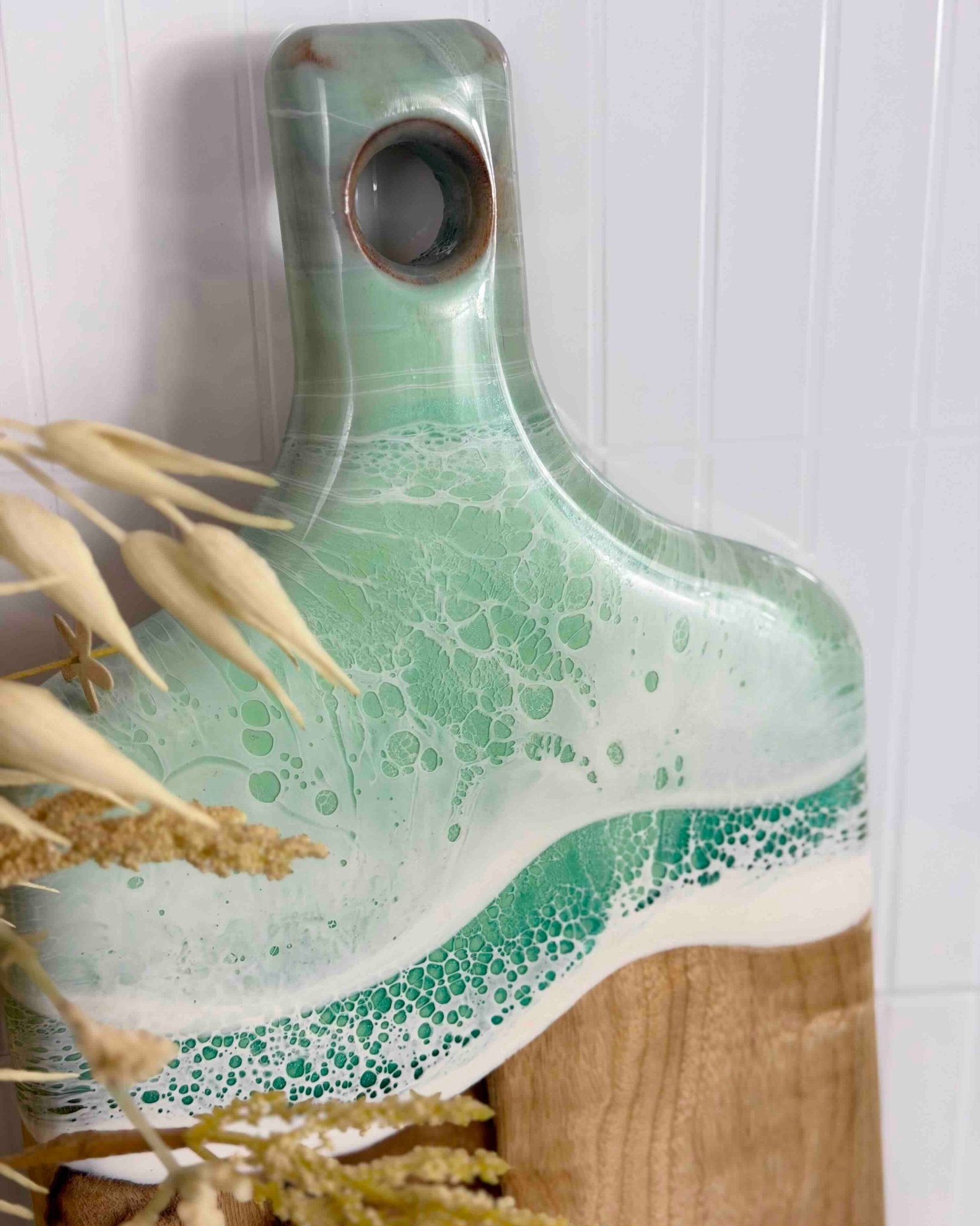 A close up shot of a chopping board with mint ocean resin wave on a white background