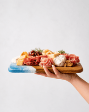 Hand holding the mini charcuterie board with various meats, cheeses, and fruits on a light gray background
