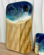 Wooden cutting board with a wavy edge, and a hanging hole cutout, with blue and white rolling resin waves