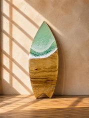 The mini surfboard cheeseboard leaning against the kitchen wall with the mint green resin waves on the tip 