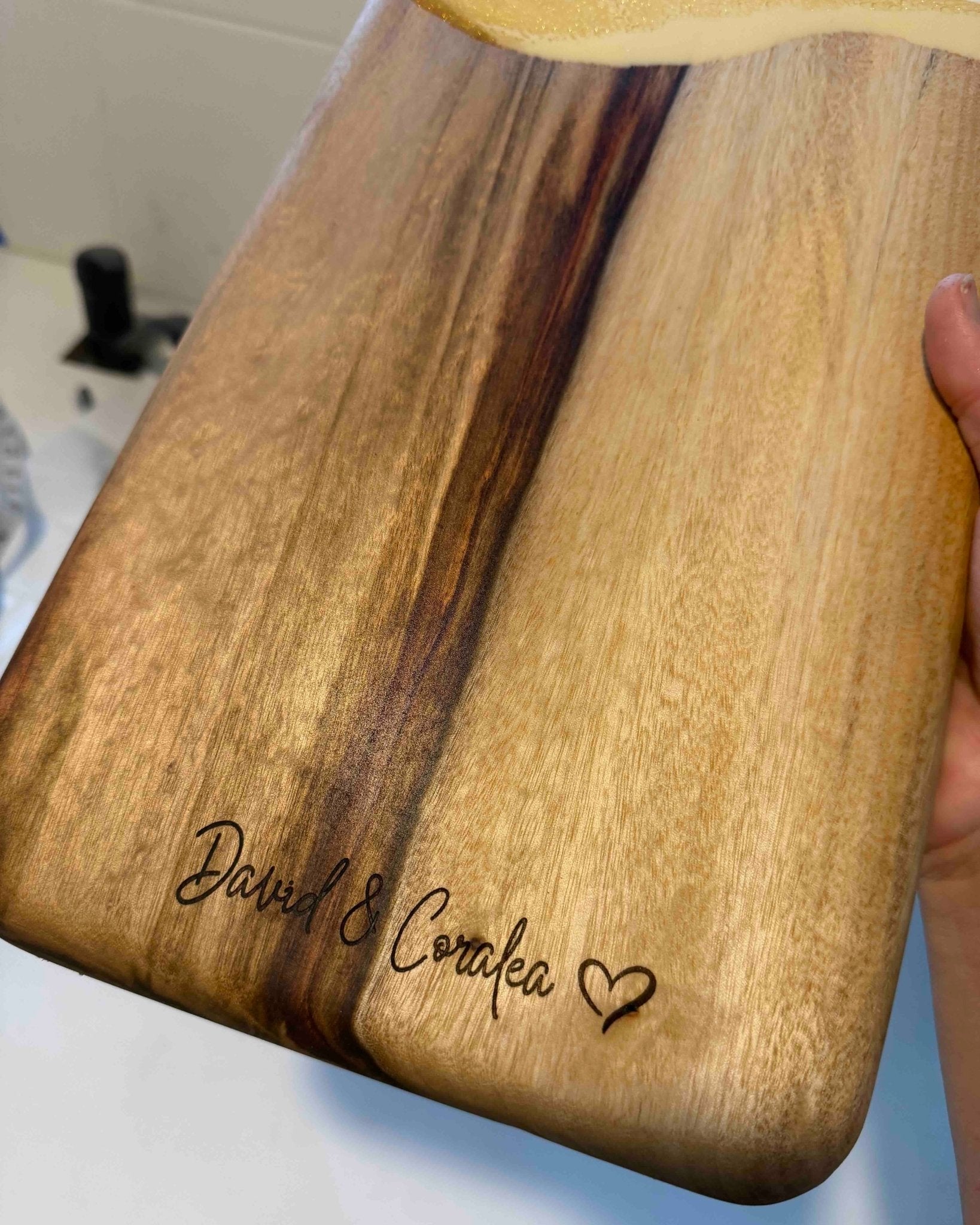 Wooden cutting board with engraved text featuring a couples two names and a heart symbol
