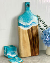 Wooden cutting board with blue wave resin handle on a kitchen counter with a matching coaster set 
