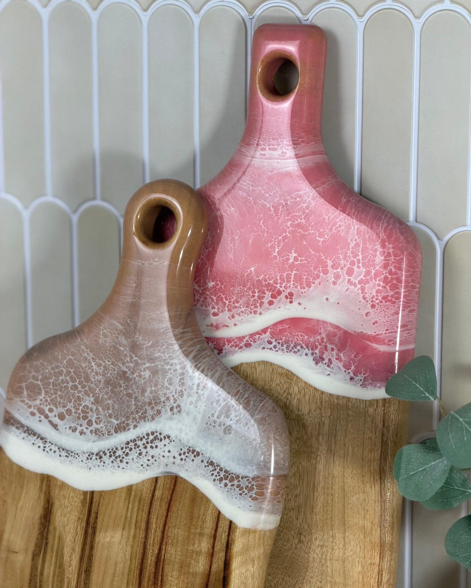 Two resin covered cutting boards with a pink and brown gradient on a wooden timber surface.