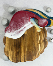 Resin santa shaped cheeseboards in 4 colours on a silver background with silver christmas baubles 