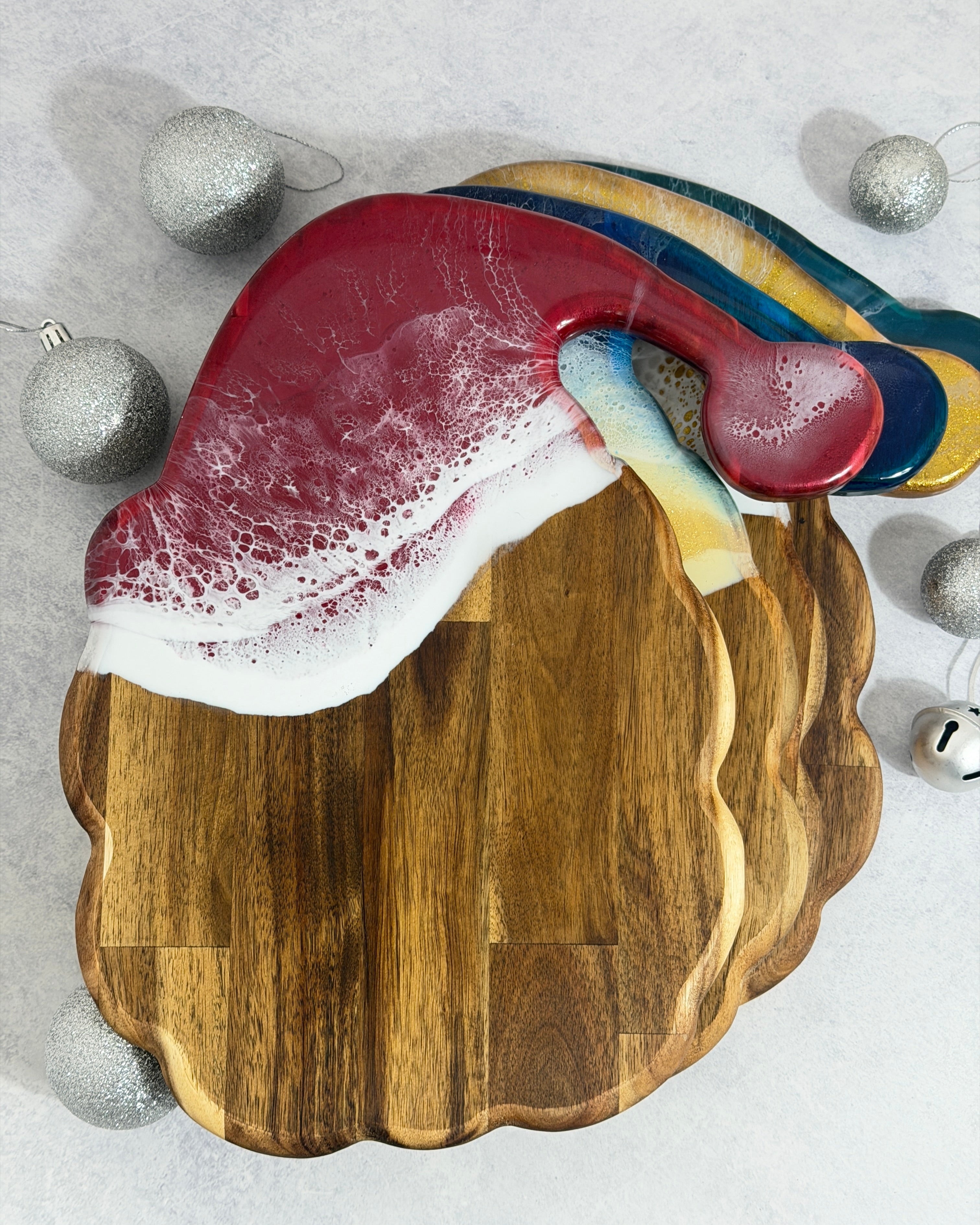 Resin santa shaped cheeseboards in 4 colours on a silver background with silver christmas baubles 