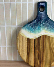 A round paddle board in the beach coloured resin shot in against a kitchen splashback, in a close up showing the detail of the resin waves