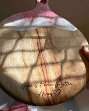 A round paddle cheeseboard with pink and white resin rolling waves and engraved memorial text for Henry
