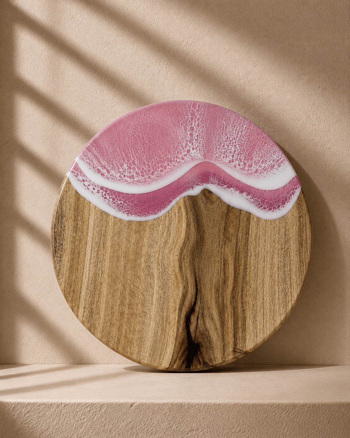 Round wooden serving board with a wavy pink and white resin inlay, displayed on a beige pedestal with soft window shadow overlays.