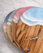 Wooden cheeseboards with resin ocean waves in 4 colours design on a light grey surface
