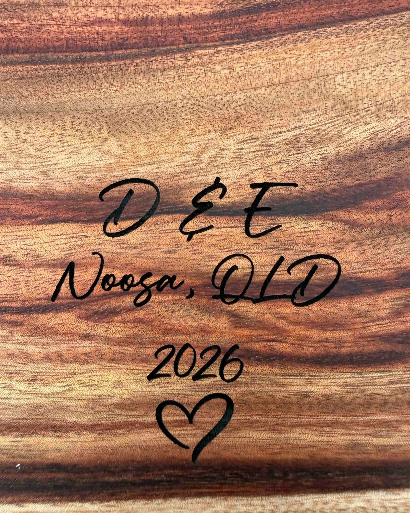 Wooden surface with text 'D & E Noosa, QLD 2026' and a heart symbol.