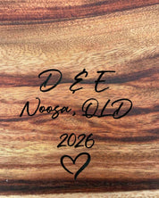 Wooden surface with text 'D & E Noosa, QLD 2026' and a heart symbol.