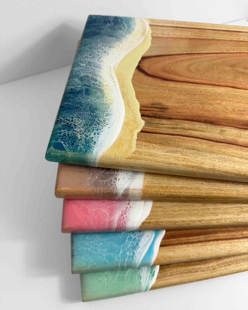 A pile of square resin ocean cheeseboards on a white background