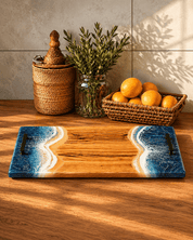Wooden cutting board with ocean epoxy waves on a wooden surface with decorative items.